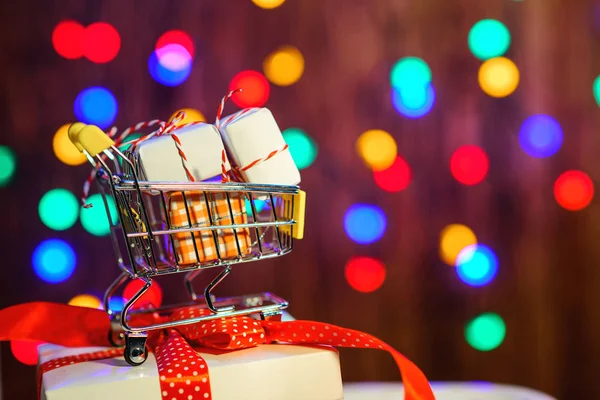 Shopping cart with Christmas box. Valentine\'s gifts. Color bokeh background. Christmas sales. Merry Christmas and Happy New Year. Gifts and shopping time. Buying gifts. Holidays festive shopping