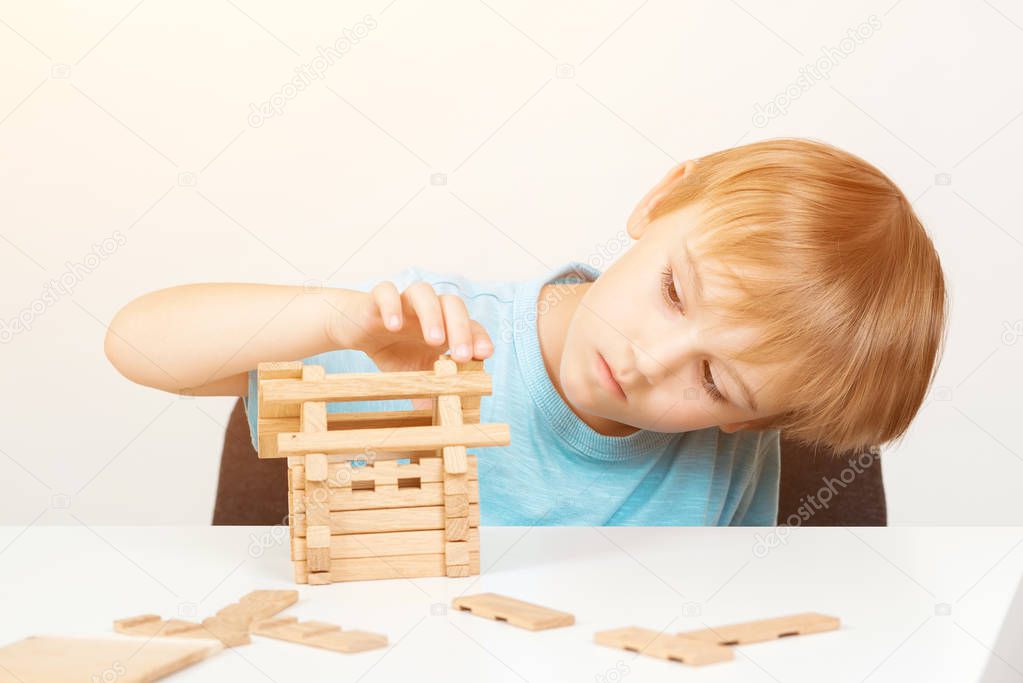 Kid builds small wooden house. Eco house. Construction concept. Little boy plays with blocks. Childhood and development. Cute kid playing at home. Smart boy create construction with wooden blocks