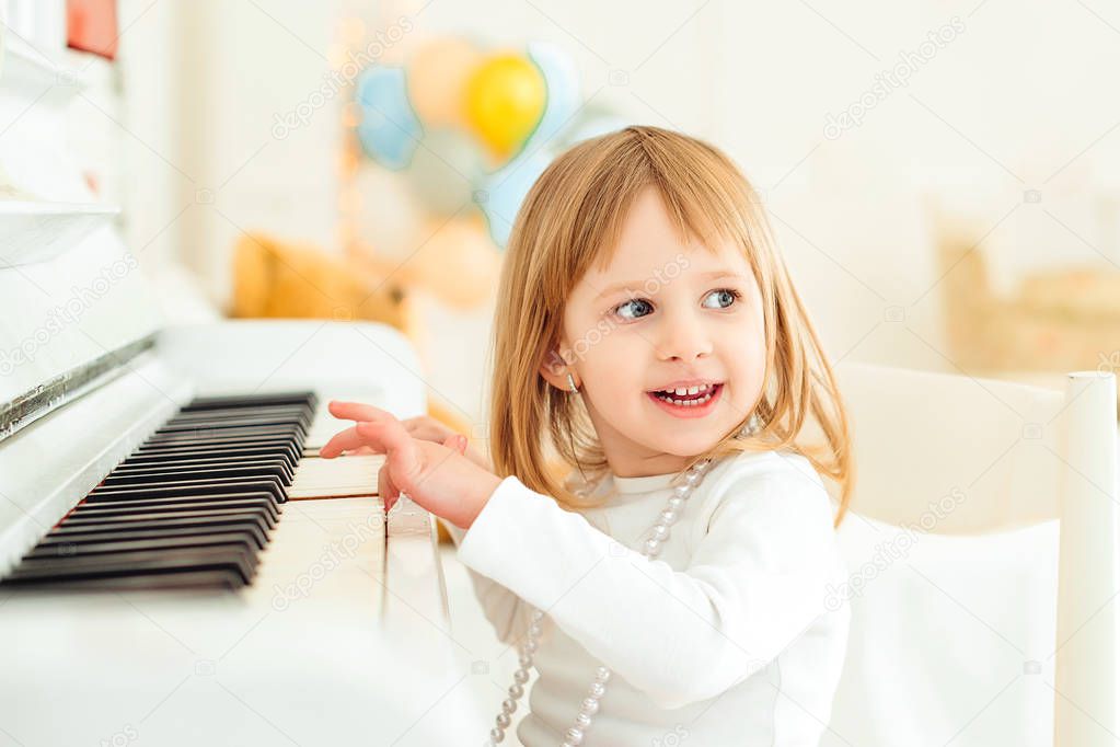 Happy child playing piano at modern class. Little girl at musical school. Education, skills concept. Preschool child learning to play music instrument. Happy childhood. Child smiling at class.