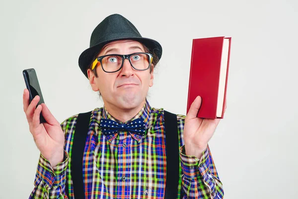 Funny nerd with glasses with book and mobile phone. Playful man in checkered shirt and black hat. Excited man having an idea. Male nerd with funny face over white background