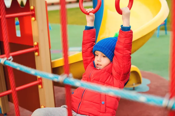 幸せな子供の屋外の遊び場で楽しい時を過します 暖かい服を着てかわいい男の子 面白い子は冷たい秋の野外で遊ぶ 子供とレジャー カラフルなモダンな遊び場 幸せな子供時代 — ストック写真