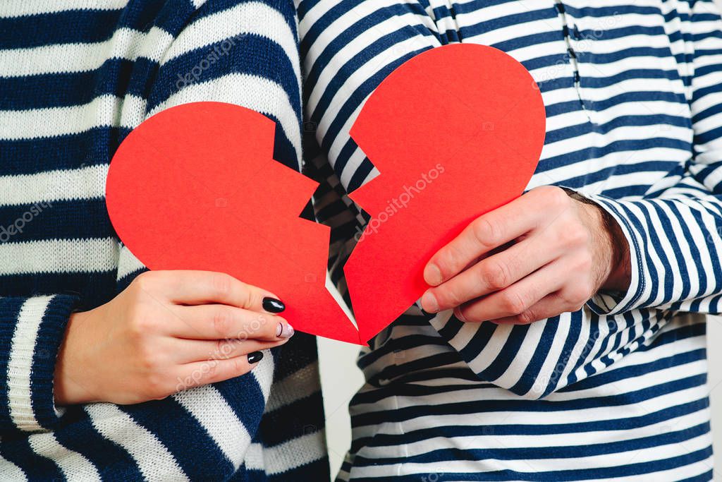 Young couple with broken heart, close up. Unrequited love. Broken heart. Love and relationship problems concept. Man and woman hands holding two parts of broken heart. Unhappy Valentine Day