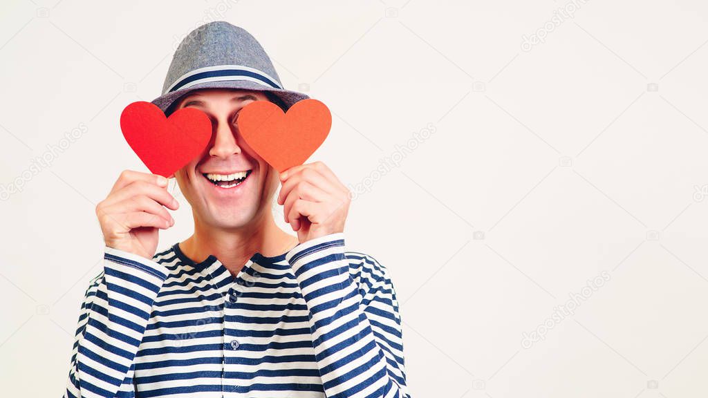 Happy Valentines Day. Funny man covers eyes with red hearts. Happy man in love. Romantic guy holds valentine cards. Be my valentine. Boyfriend showing love fun affection. Copy space.