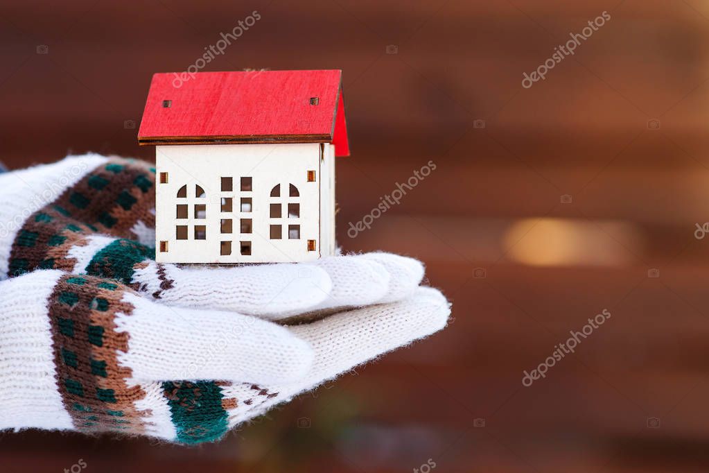 Model of house at hands, outdoors. Protecting and isolating house. Winter. Real estate and property concept. Small miniature of house at hands in winter gloves. Preparing the house for winter time