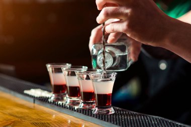 Barman make alcoholic shots in nightclub. Strong alcoholic drink. Multicolored shots on the bar. Small glasses with alcoholic drinks at bar counter. Party at nightclub clipart
