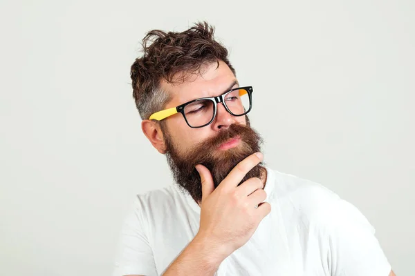 Hipster hombre pensando, tocándose la barba. Tipo barbudo en gafas reflexivo, sobre fondo blanco . — Foto de Stock