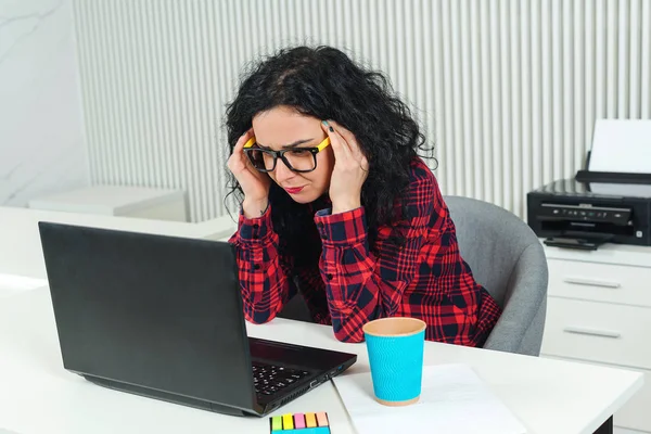 Müde Geschäftsfrau am Arbeitsplatz. Gestresste Frau arbeitet im modernen Büro am Laptop. — Stockfoto