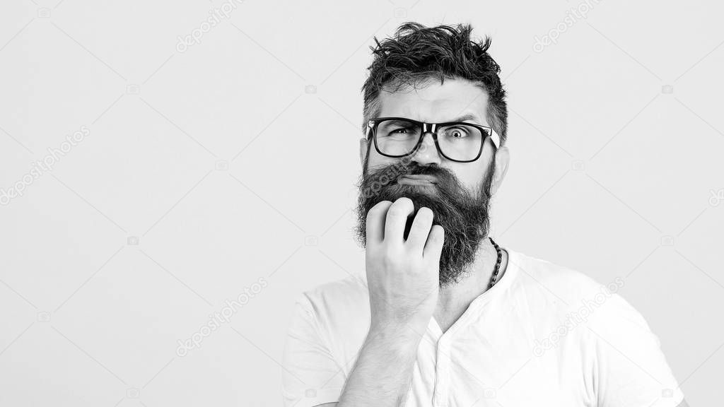 Pensive man touching his beard on white wall. Handsome man in glasses thinks. 