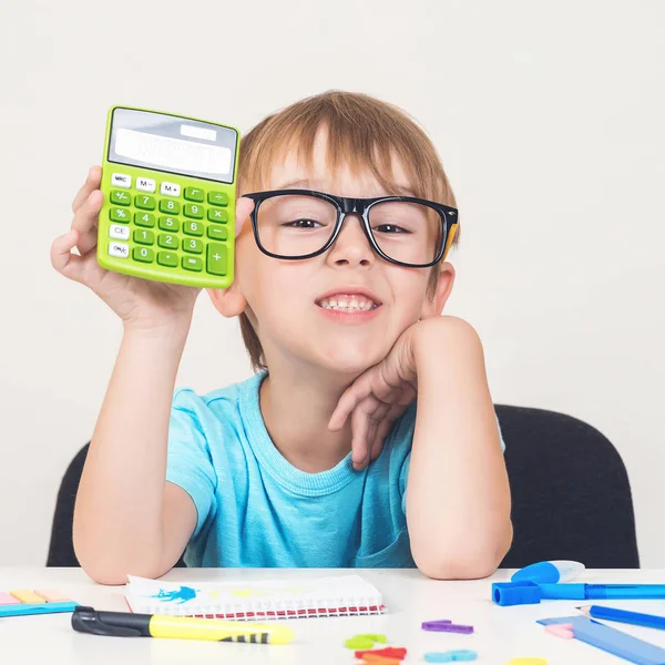 Joven estudiante sosteniendo calculadora. Un niño con gafas sentado en el escritorio. Educación y desarrollo . — Foto de Stock
