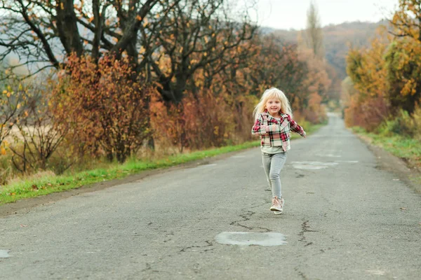 Uma menina a correr pela estrada no Outono. Menina feliz criança com cabelos longos ao ar livre . — Fotografia de Stock