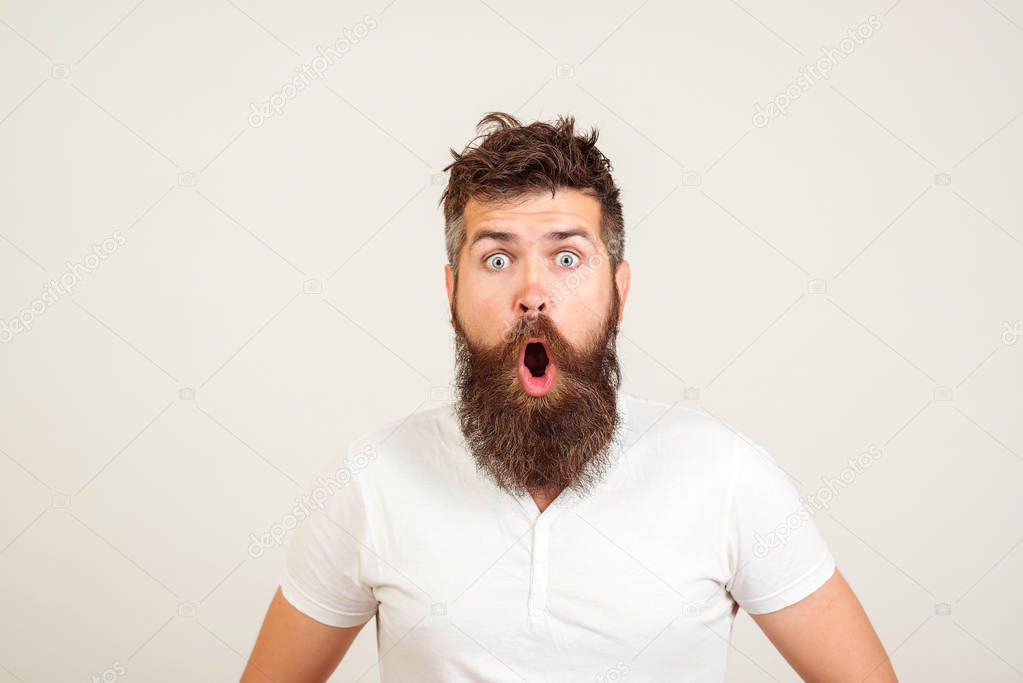 Shocked bearded man stares at camera. Bearded hipster guy widely opened mouth and eyes. 