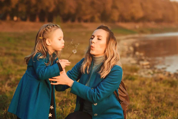 Matka s malou dcerou fouká v přírodě na pampeliška. Šťastný koncept rodiny, dětství a životního stylu. — Stock fotografie