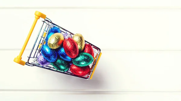 Mini carrito de compras lleno de huevos de chocolate de Pascua. Feliz Pascua. Vista superior, espacio de copia . — Foto de Stock