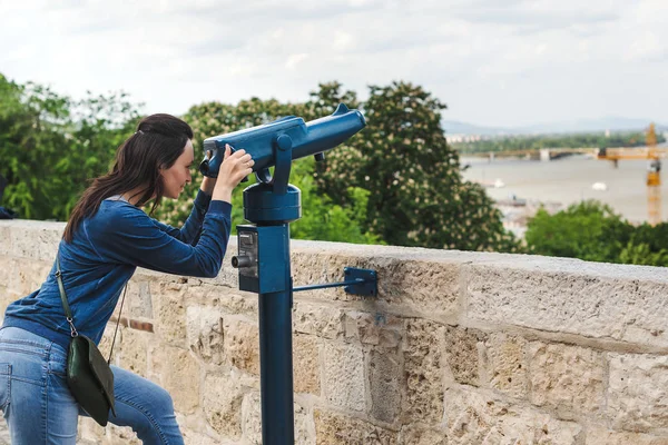 Travel tourist woman on Europe holidays. Hipster girl using telescope looks panorama of the city.