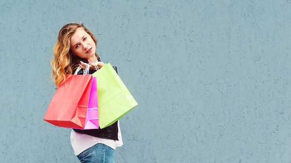 Mujer de compras sosteniendo bolsas de color. Chica posando sobre fondo gris, espacio de copia . — Foto de Stock