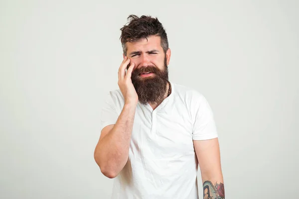 Homem barbudo triste com dor de dente, no fundo branco. Conceito de dor de dente. Jovem frustrado a tocar na bochecha e a manter os olhos. Homem sentindo dor, sofrendo de dor de dente ruim . — Fotografia de Stock