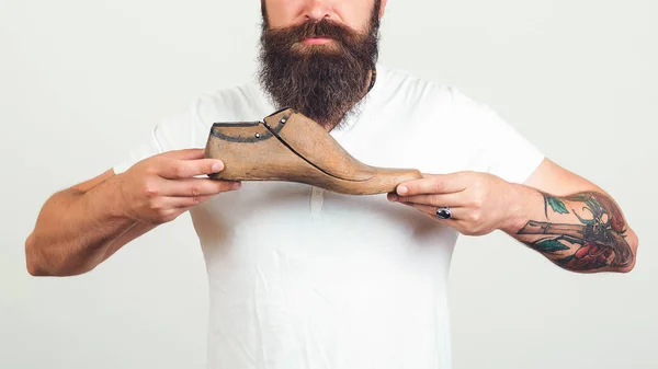 El modelado del diseño de los zapatos. Joven diseñador sosteniendo un último zapato de madera sobre fondo blanco . — Foto de Stock