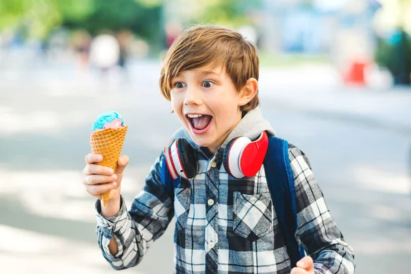 Happy kid eating ice cream at the city centre. Stylish boy 8 years old walking on street. Emotional child holding ice cream.