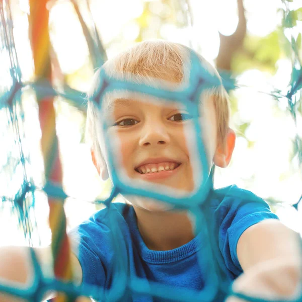 Happy child climbing on a playground ropes. Cheerful little boy playing on modern playground. — Stock Photo, Image