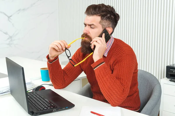 Selbstbewusster bärtiger Mann, der am Laptop arbeitet. Mann telefoniert. bärtiger Typ an seinem Arbeitsplatz im Büro. — Stockfoto