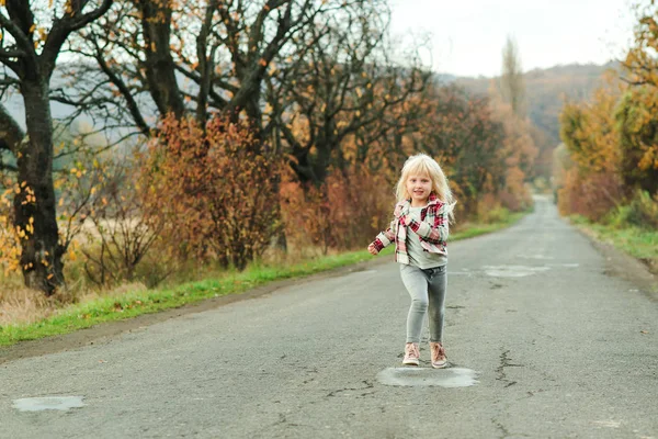 Menina feliz correndo na estrada na época do outono. Criança de moda elegante ao ar livre. Férias de outono . — Fotografia de Stock