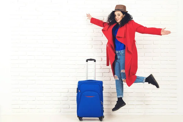 Woman traveler with suitcase on white brick background. Happy girl ready for trip. Travelling and lifestyle concept.