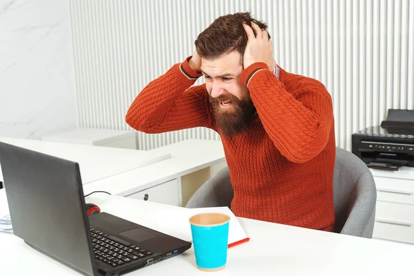 Homem barbudo estressado segurando a cabeça com a mão no local de trabalho. Homem olhando para laptop . — Fotografia de Stock