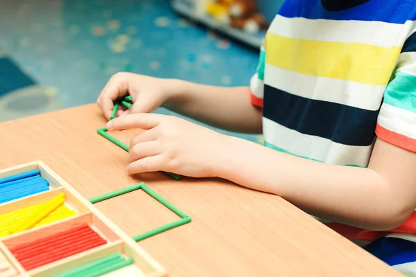 Kind fertigt aus bunten Stöcken geometrische Formen. Vorschulerziehung und Entwicklung. Grundschulklasse. — Stockfoto