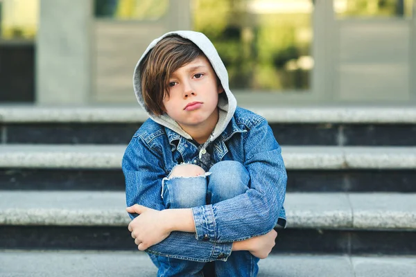 Trieste jongen zit op de trap, voor school. Alleen ongelukkig kind in de straat van de stad. — Stockfoto