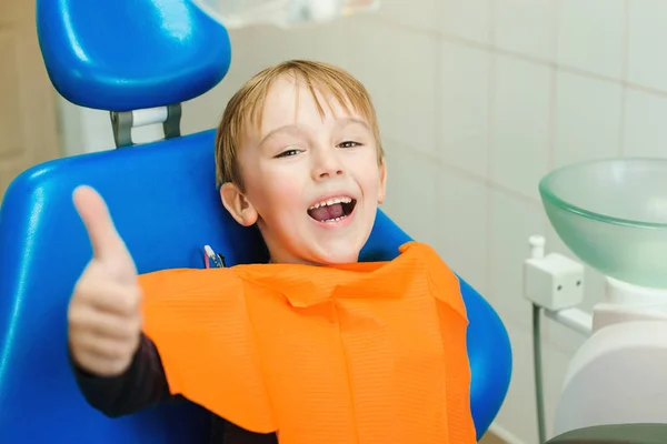 Um menino feliz a visitar o dentista. Criança sentada em uma cadeira azul dental. Examinando os dentes do menino na clínica dentária — Fotografia de Stock