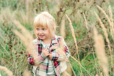 Modaya uygun küçük kız kırsal kesimde yürüyor. Mavi gözlü ve sarı saçlı mutlu bir kız. Çocuk modası. 