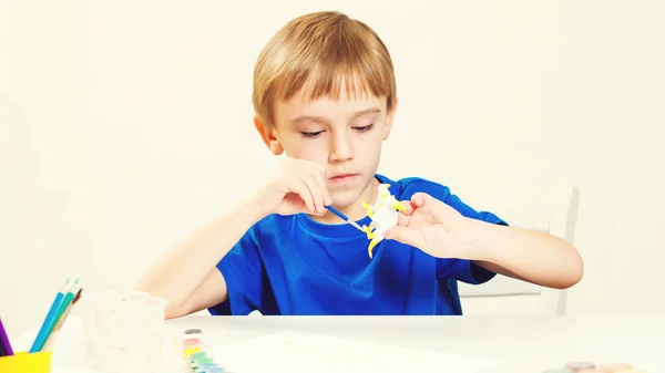 El niño pinta en la clase de arte. Concepto de creatividad y educación. Chico pinta dinosaurio figura pequeña. Estudio de niños . — Foto de Stock