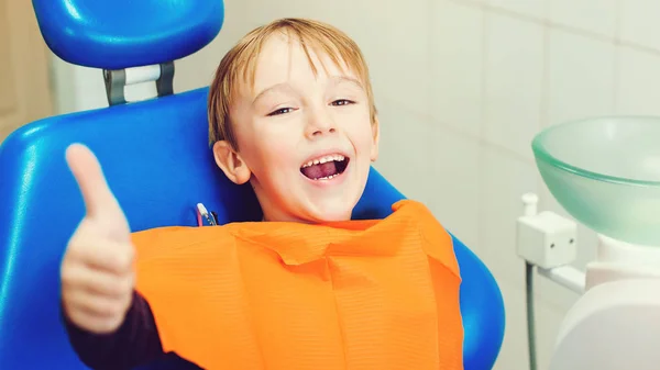 Dentista examinando los dientes de un niño en la clínica. Feliz chico sentado en la silla dental. Niño durante el tratamiento de sus dientes por el dentista —  Fotos de Stock