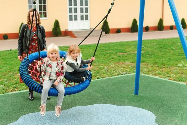 Glada systrar och ung mamma har roligt tillsammans. Mamma driver skrattande döttrar på swing. — Stockfoto