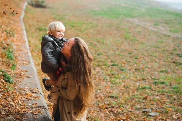 Šťastná matka a chlapeček hrají a smějí se na podzimní procházce. Mladá rodina na podzimní procházce. — Stock fotografie