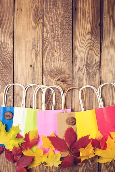 Vente d'automne. Sacs en papier couleur shopping et feuilles tombées sur fond bois. Espace de copie. Rabais d'automne . — Photo