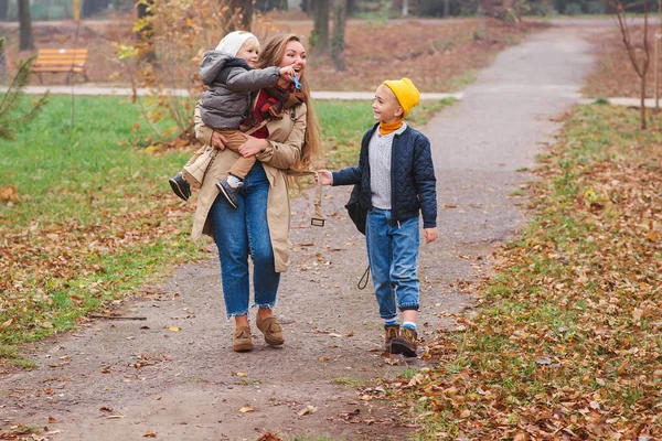 Madre y sus hijos se divierten al aire libre. Vacaciones de otoño. Paseo familiar joven en el parque de otoño. Familia, maternidad, estilo de vida y concepto de moda — Foto de Stock