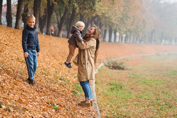 Família feliz desfrutando dia de outono. Jovem mãe e crianças em passeio de outono no parque . — Fotografia de Stock