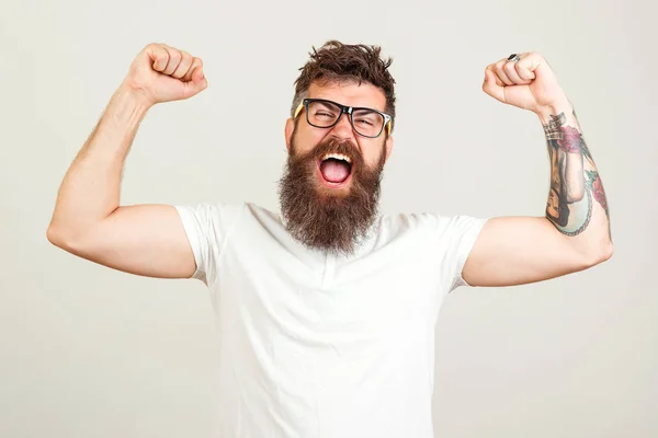 Gritando hombre brutal barbudo con las manos en alto. Emocionado hombre barbudo en gafas celebrando el éxito. Objetivo, ganador, celebrando. hipster barbudo con tatuaje . — Foto de Stock