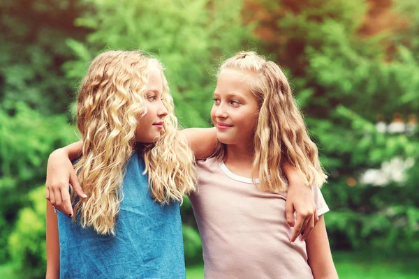 Glückliche Zwillingsschwestern, die sich im Freien umarmen. Familienspaziergang im Sommerpark. fröhliche Mädchen, die Spaß beim Spaziergang in der Natur haben — Stockfoto