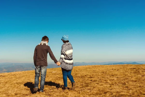 Felice giovane coppia godendo la natura in vetta alla montagna. Coppia amorevole che si tiene per mano su sfondo cielo blu . — Foto Stock