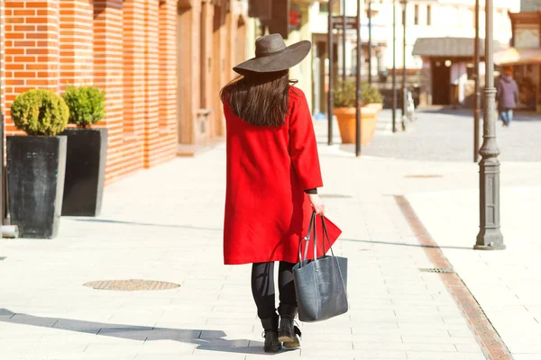 Elegante hermosa mujer caminando en la calle. Chica con abrigo rojo, sombrero negro y bolsa de moda. Traje de moda, tendencia de otoño, accesorios . — Foto de Stock