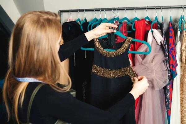 Moda dziewczyna wybiera strój na imprezę nocną. Kobieta dresmaker trzyma Wieszak z sukni. Kobieta pracuje w butiku mody. — Zdjęcie stockowe