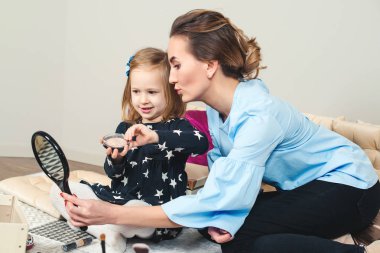 Evde makyaj yapan küçük kızı ile güzel anne. Genç Anne ve sevimli çocuk kız evde birlikte eğleniyoruz. 