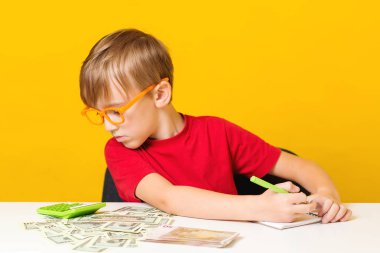 Küçük çocuk gelecek eğitim için para biriktiriyor. Finansal sorumluluk öğrenmek ve birikimleri hesaplamak. Masadaki çocuk para sayıyor.