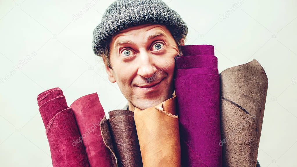 Craftsman holds set of color leather in his workshop. Master has