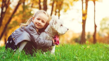 Şirin bir kız bebek köpekle sarılıp oynuyor. Çocuklar sonbahar yürüyüşünde evcil hayvanlarıyla eğlenceli oyunlar oynarlar..