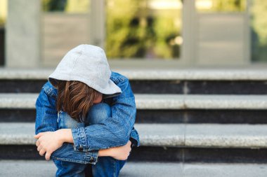 Depresyondaki çocuk okul dışında üzgün bir şekilde tek başına oturuyor. Öğrenci çocuk merdivenlerde oturup ağlıyor. Okul zorbalığı konsepti