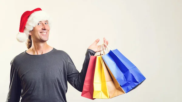 Comprador feliz segurando sacos de compras. O homem usa chapéu de Pai Natal. Tempo de Natal, venda, compras. É hora de comprar presentes de Natal. Vendas de inverno . — Fotografia de Stock