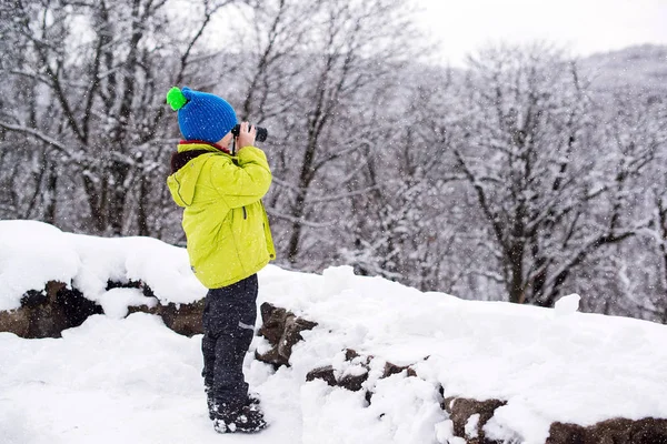 Un ragazzino che perquisisce la casa di Babbo Natale in montagna. Ragazzo che usa il binocolo e si diverte durante la passeggiata invernale nella foresta. Vacanze di Natale — Foto Stock